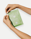 Person holding a green skincare sheet mask with a brand logo on a white background
