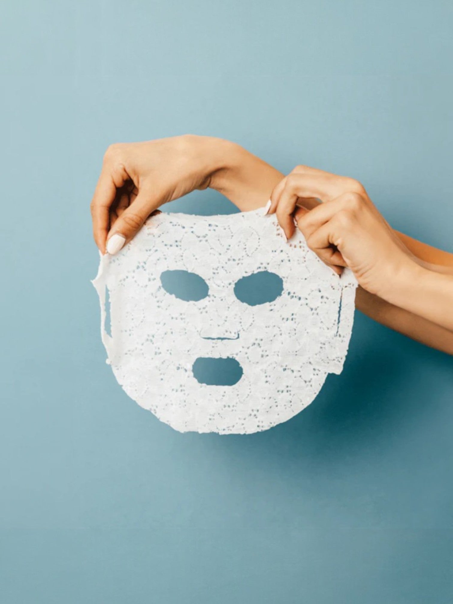 Person holding a Dermovia white face mask against a light blue background