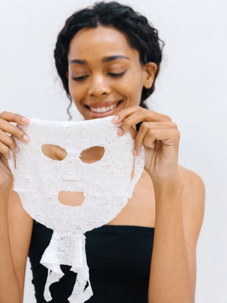 Woman holding a white face mask against a plain background