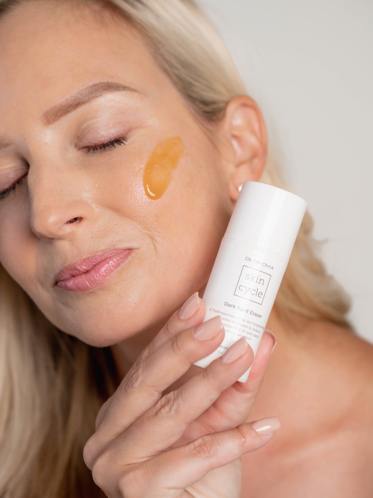 Woman applying Dermovia dark spot eraser to her face with ht eproduct in her hand.