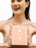 Woman holding a dermovia firming mask box with a plain background