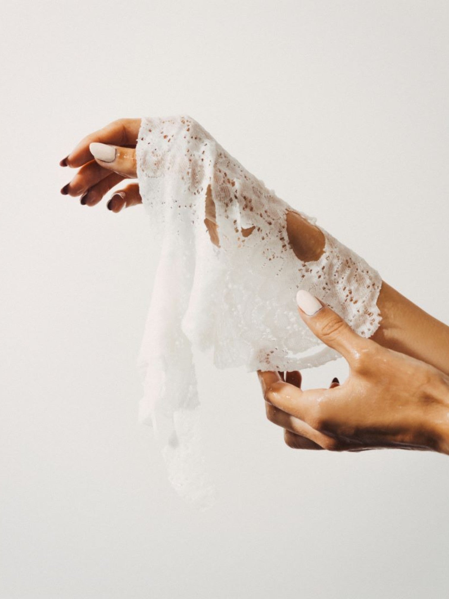 Close-up of hands holding a white lace mask against a light background